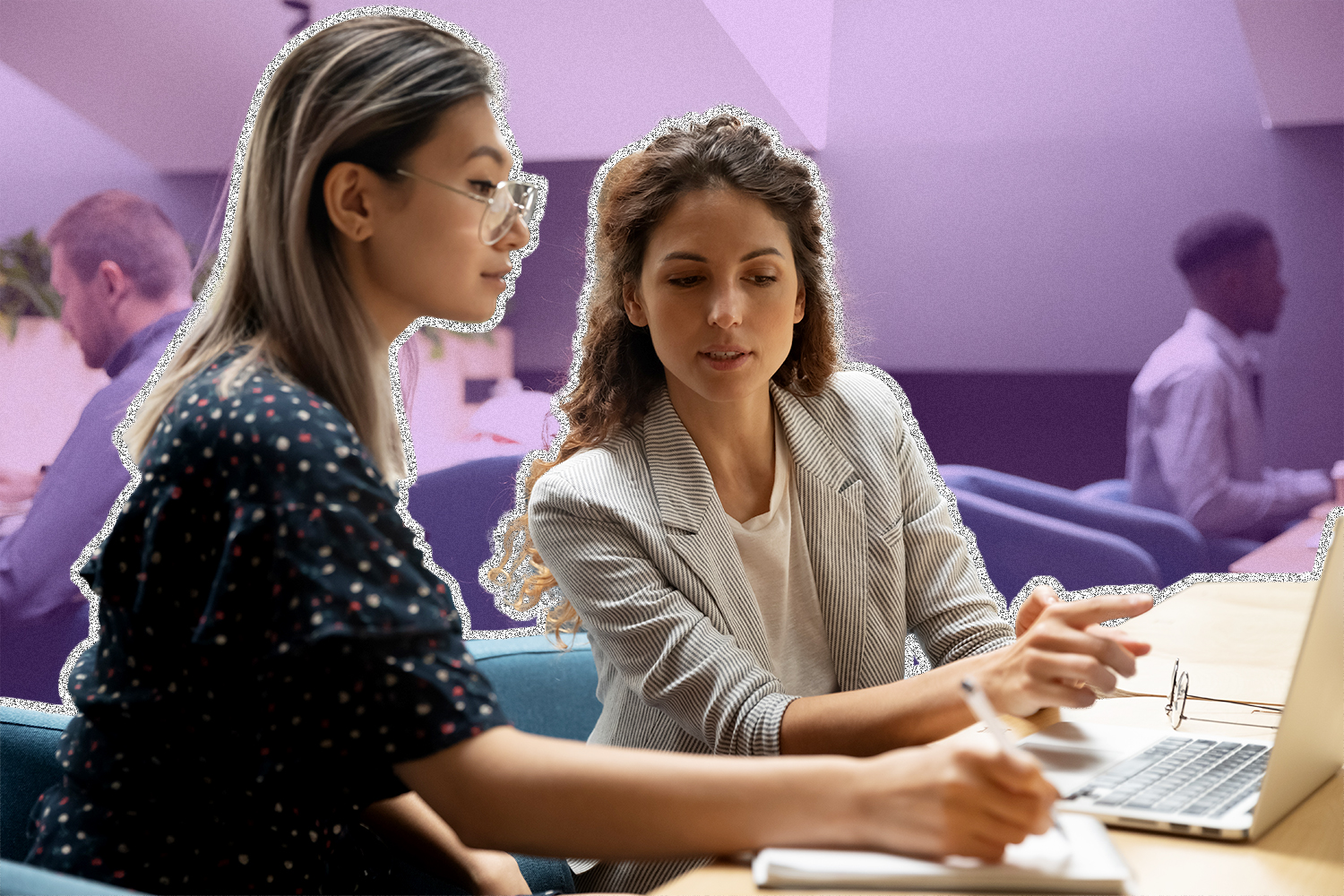 An employee points to a laptop next to another employee who writes on a notepad.