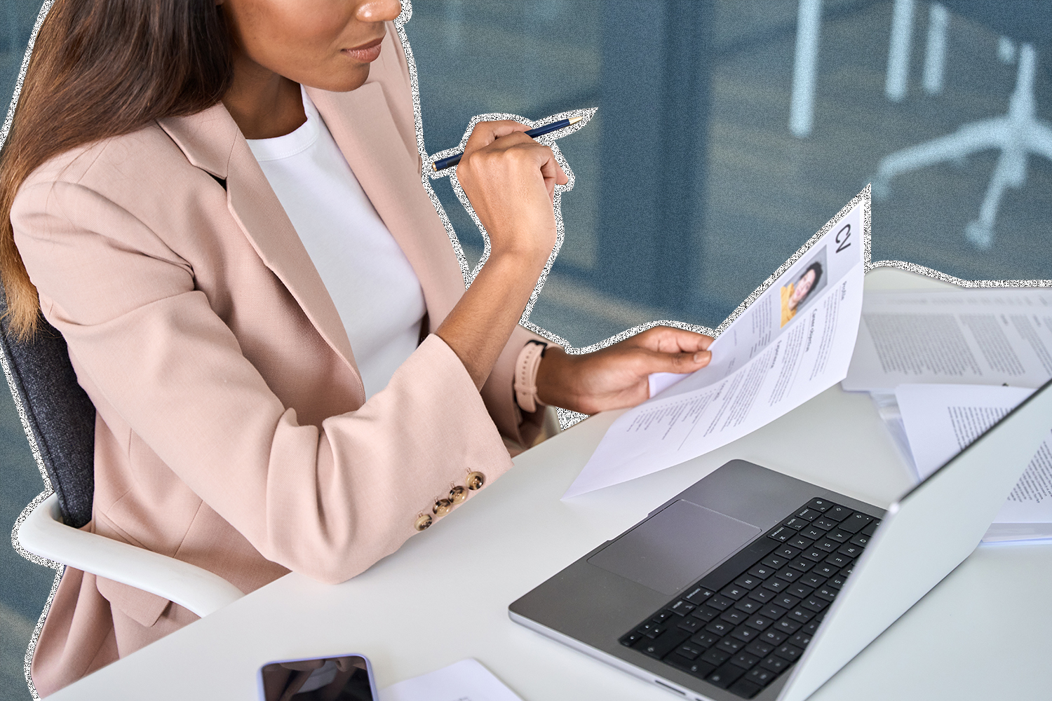 A woman holding a resume sitting at a table with a laptop on it