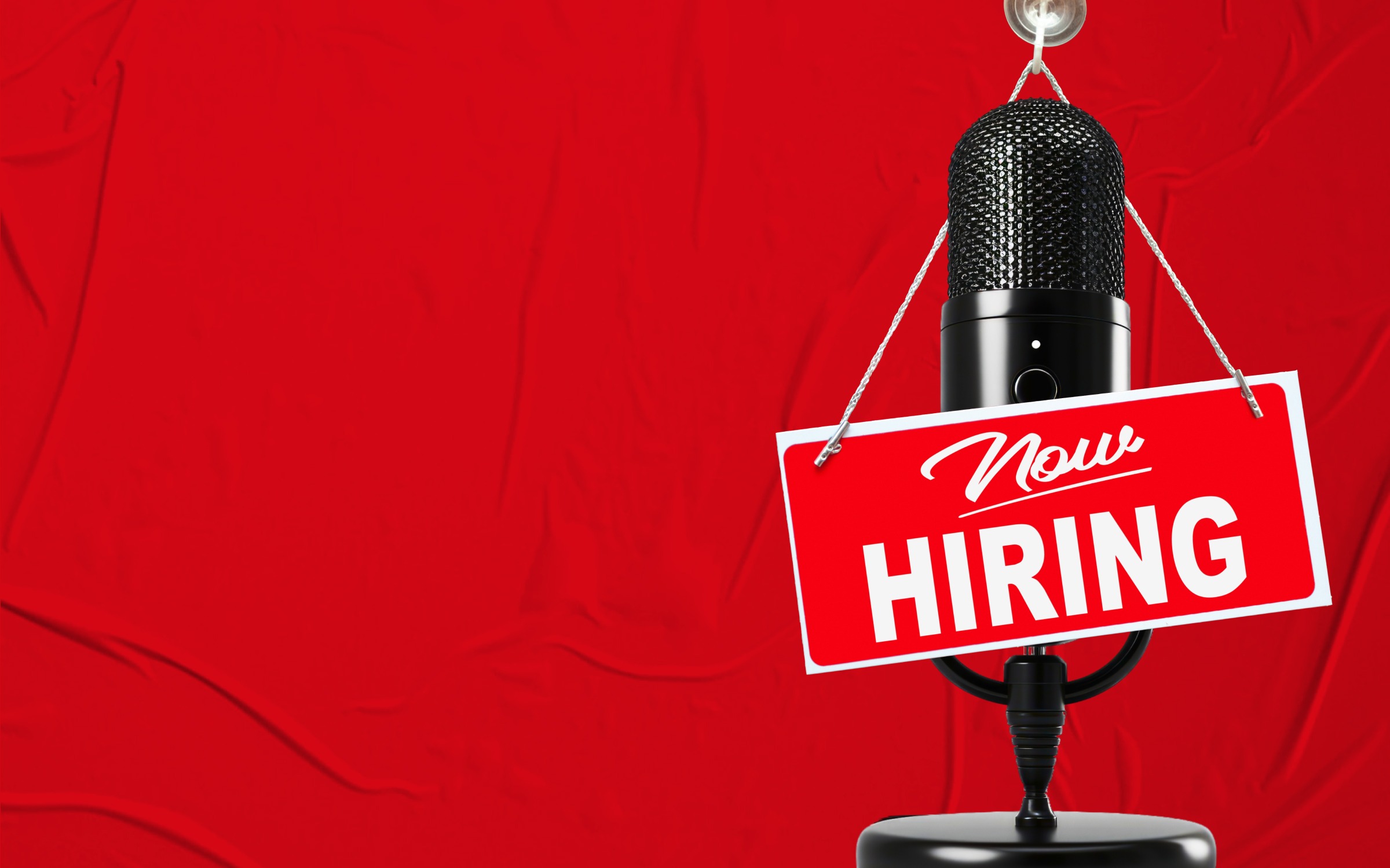 A microphone with a red and white sign hanging from it that reads "Now HIRING." The background is entirely red. This image is about job opportunities, talking about hiring or getting a job, clear and effective communication in the hiring process, and attracting potential candidates.
