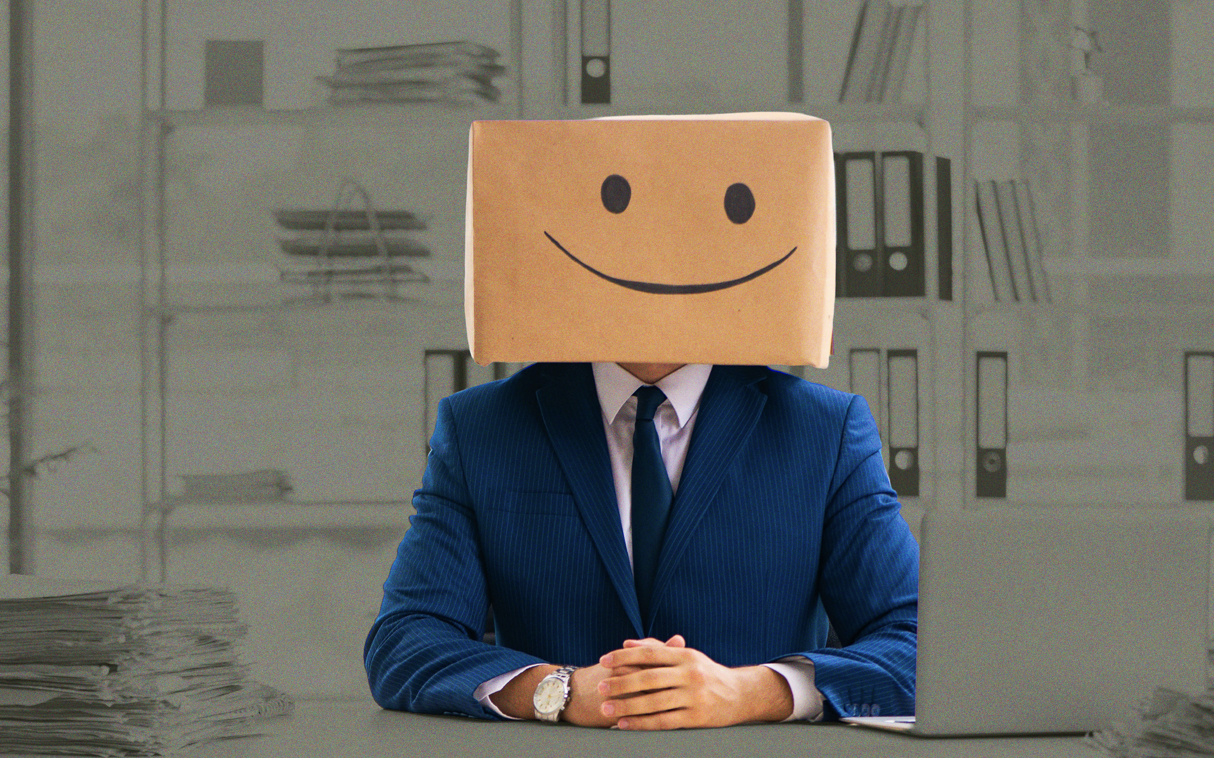 A business professional in a blue suit sits at an office desk with a cardboard box covering their head, marked with a simple smiley face. The deliberately artificial expression suggests performative positivity or compassion and the importance of authenticity, ethics and credibility in values-based marketing.